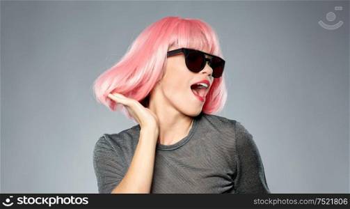 style, fashion and people concept - happy laughing young woman in pink wig and black sunglasses dancing over grey background. happy woman in pink wig and sunglasses dancing