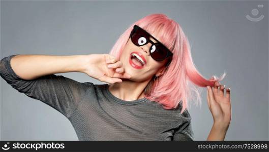 style, fashion and people concept - happy laughing young woman in pink wig and black sunglasses over grey background. happy woman in pink wig and black sunglasses