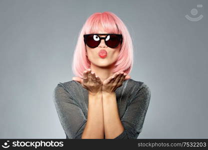 style, fashion and people concept - happy young woman in pink wig and black sunglasses sending air kiss to camera over grey background. woman in pink wig and sunglasses sending air kiss