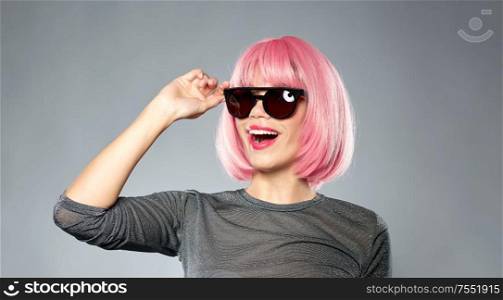 style, fashion and people concept - happy young woman in pink wig and black sunglasses over grey background. happy woman in pink wig and black sunglasses