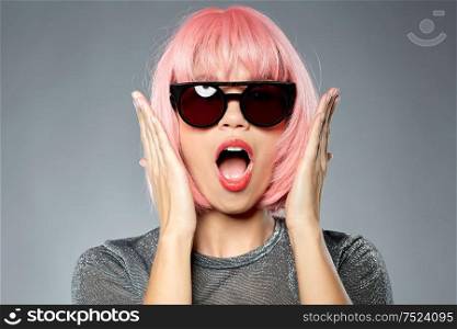 style, fashion and people concept - shocked young woman in pink wig and black sunglasses over grey background. happy woman in pink wig and black sunglasses