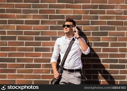 style, music, technology and people concept - happy smiling young man in headphones and sunglasses with bag over brickwall