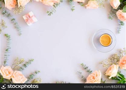 Styled desktop scene. Cup of coffee with gift or present box and flowers on blue background from above, copy space