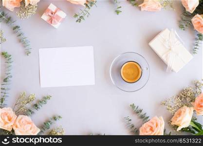Styled desktop scene. Cup of coffee with gift or present box and flowers on blue table from above, copy space on blank paper card