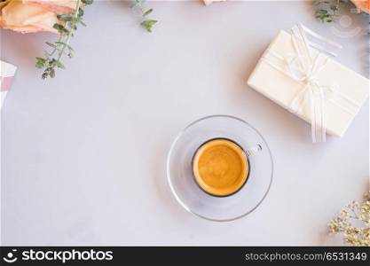 Styled desktop scene. Cup of coffee with gift or present box and flowers on blue table from above