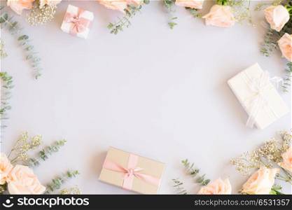 Styled desktop scene. gift or present boxes and flowers frame on blue background from above, copy space