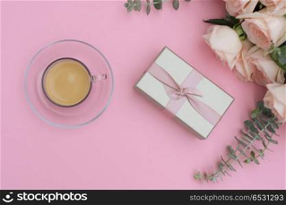 Styled desktop scene. Morning cup of coffee with gift or present box and rose flowers on pink table from above, flat lay scene