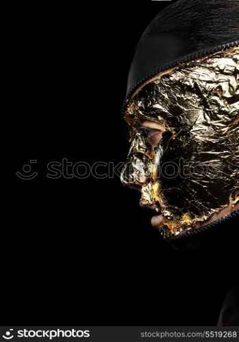 Styled Woman&#39;s Face Covered Golden Foil over Black Background. Mystery