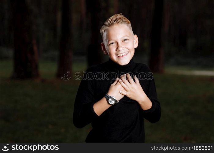 Stylish attractive young guy with a fashionable hairstyle in a trendy black outfit enjoys an outdoor vacation in the park. smiling boy.. Stylish attractive young guy with a fashionable hairstyle in a trendy black outfit enjoys an outdoor vacation in the park. smiling boy