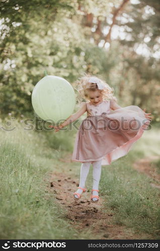 Stylish baby girl 4-5 year old holding big balloon wearing trendy pink dress in meadow. Playful. Birthday party. little girl with a balloon in the park. Stylish baby girl 4-5 year old holding big balloon wearing trendy pink dress in meadow. Playful. little girl with a balloon in the park. Birthday party.