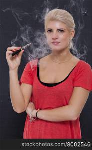 Stylish blond woman smoking an e-cigarette exhaling a cloud of smoke with her eyes closed in enjoyment, profile view on a dark background