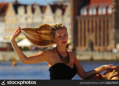 Stylish blonde traveler woman outdoors in european city, old town Gdansk in the background, Poland Europe
