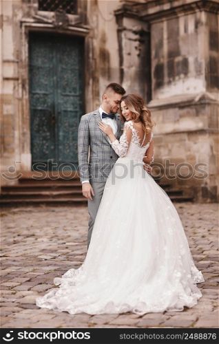 Stylish bride and groom gently hugging in european city street. Gorgeous wedding couple of newlyweds embracing near ancient building. Romantic moment. wedding day.. Stylish bride and groom gently hugging in european city street. Gorgeous wedding couple of newlyweds embracing near ancient building. Romantic moment. wedding day