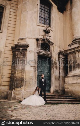 Stylish bride and groom gently hugging on european city street. Gorgeous wedding couple of newlyweds embracing near ancient building. romantic sensual moment of newlyweds.. Stylish bride and groom gently hugging on european city street. Gorgeous wedding couple of newlyweds embracing near ancient building. romantic sensual moment of newlyweds