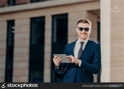Stylish business owner in trendy sunglasses uses modern digital tablet for taking part in online conference with business partners, has positive smile on face, connected to wireless internet