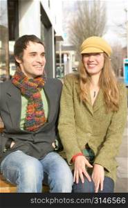 Stylish Caucasian Couple Sitting On A Bench And Laughing