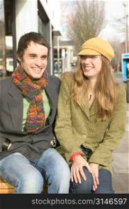 Stylish Caucasian Couple Sitting On A Bench And Laughing