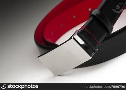 Stylish coiled mens black leather belt with a brushed metal silver buckle and colorful crimson lining, close up view on a graduated grey background