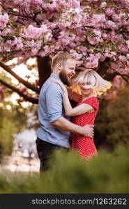 Stylish couple near the Sakura tree. beautiful young couple, man with beard and blonde woman hugging and haning fun in the spring park