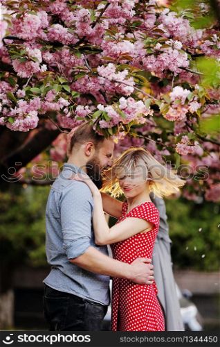 Stylish couple near the Sakura tree. beautiful young couple, man with beard and blonde woman hugging and haning fun in the spring park. Concept spring. fashion and beauty