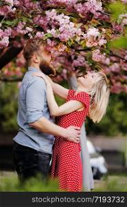 Stylish couple near the Sakura tree. beautiful young couple, man with beard and blonde woman hugging and haning fun in the spring park. Concept spring. fashion and beauty