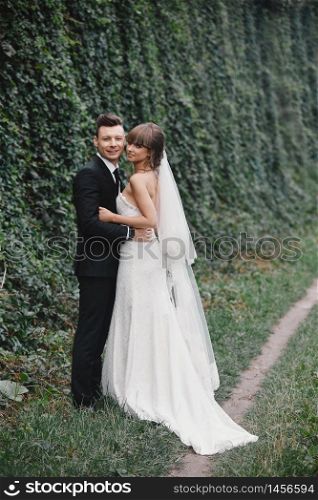 Stylish couple of newlyweds on their wedding day. Happy young bride, elegant groom and wedding bouquet. Portrait of young wedding couple at nature.