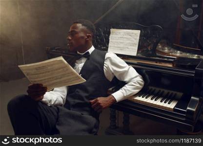 Stylish ebony grand piano player, jazz performance in club. Negro performer poses at musical instrument before playing melody. Stylish ebony grand piano player, jazz performance