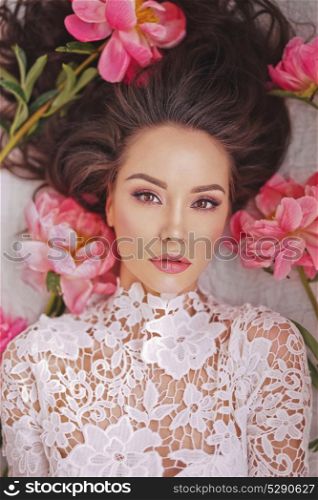 Stylish fashion photo of beautiful young woman lies among peonies. Holidays and Events. Valentine?s Day. Spring blossom. Summer season