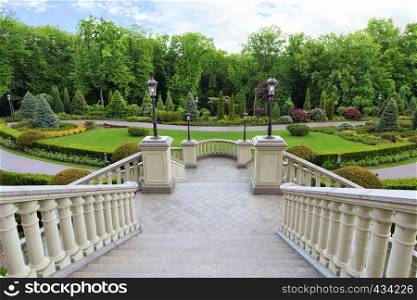 Stylish granite staircase with a balustrade with beautiful carved balusters in classic style, overlooks the beautiful lawn of a magnificent garden.. Beautiful granite staircase with a carved balusters