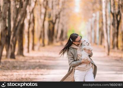 Stylish happy young woman wearing jeans, white sneakers walking with white puppy. Young stylish woman walking with white dog