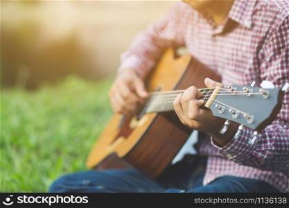Stylish hipster guy Acoustic Guitar Playing by hand. Artist Men musician Playing Acoustic Guitar in public park