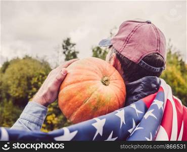 Stylish man in a denim shirt holding a ripe, yellow pumpkin against the sky and green trees. View from the back. Preparing for the holidays. Stylish man holding a ripe, yellow pumpkin