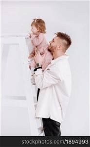 stylish man is having fun with cute child baby girl in decorated studio. daughter tries to climb the ladder. Love parenthood childhood concept. father&rsquo;s day, love care, deep devotion relationships.. stylish man is having fun with cute child baby girl in decorated studio. daughter tries to climb the ladder. Love parenthood childhood concept. father&rsquo;s day, love care, deep devotion relationships