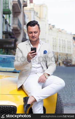 Stylish man using smartphone near sport car