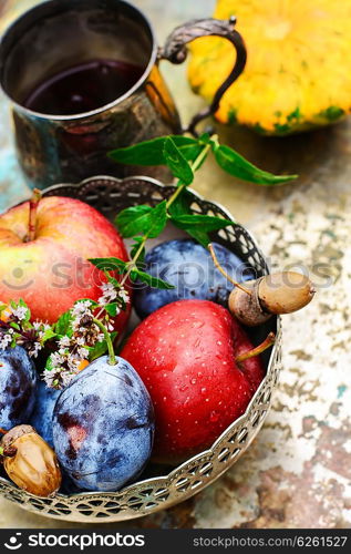 Stylish metal bowl with apples,plums and acorns in the autumn still life