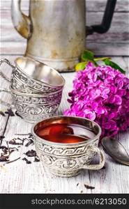 Stylish metal cup of tea. Aromatic spring tea fashion in an iron mug and a branch of a blossoming lilac