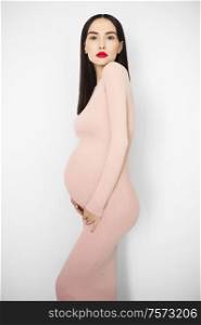 Stylish photo of elegant pregnant brunette woman in beige dress. Beautiful pregnancy. Love and care