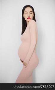 Stylish photo of elegant pregnant brunette woman in beige dress. Beautiful pregnancy. Love and care