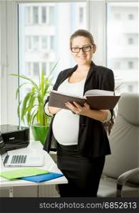 Stylish pregnant businesswoman posing with files at office