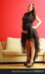Stylish pretty girl in black evening dress. Pregnant woman preparing for event. Glamour look. Prospective mothering concept.