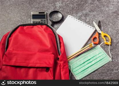Stylish red school bag backpack on a table desk with face mask protection and stationery accessory, Back to school education new normal during outbreak COVID-19 or coronavirus concept