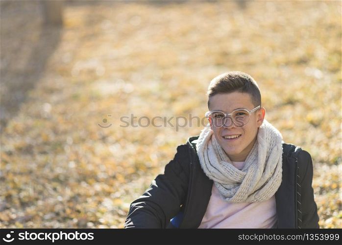 Stylish smiling teenager sitting on the ground in a city park