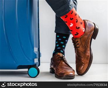 Stylish suitcase, men&rsquo;s legs, multicolored socks and new shoes on a white, isolated background. Close-up, indoors. Studio foto. Concept of style, fashion, beauty and vacation. Stylish suitcase, men&rsquo;s legs and bright socks