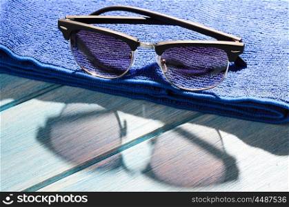 stylish sunglasses and towel on table. stylish sunglasses and towel on blue wooden table with sunlight