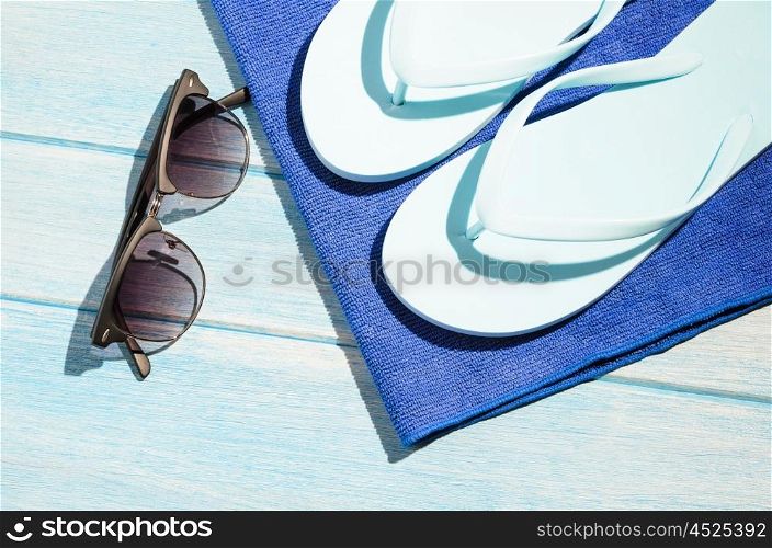 stylish sunglasses with flip flops and towel. stylish sunglasses with flip flops and towel on blue wooden table with sunlight