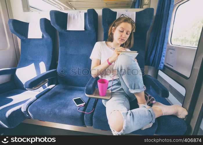 Stylish teenage girl is going by train. Draws and listens to music