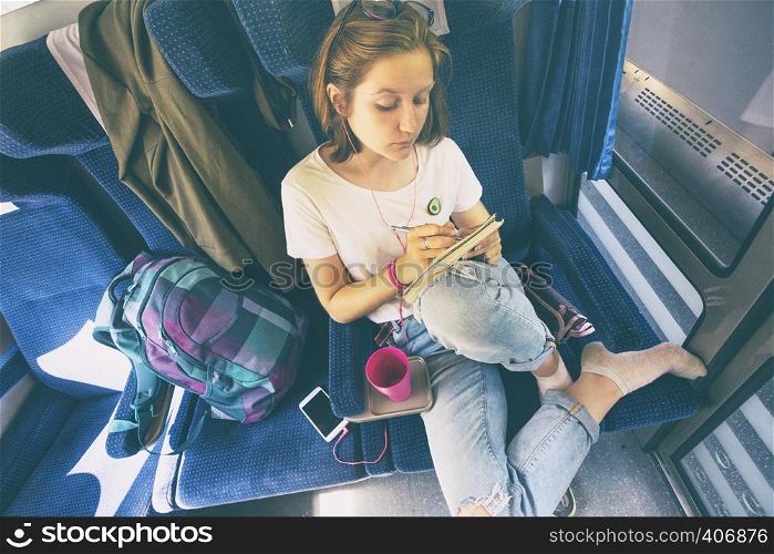 Stylish teenage girl is going by train. Draws and listens to music