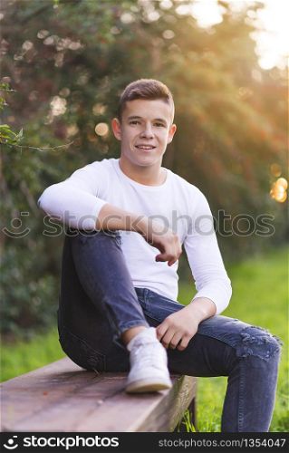 Stylish teenager sitting on a wooden bench on a city park