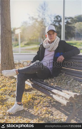 Stylish teenager sitting on a wooden bench on a city street