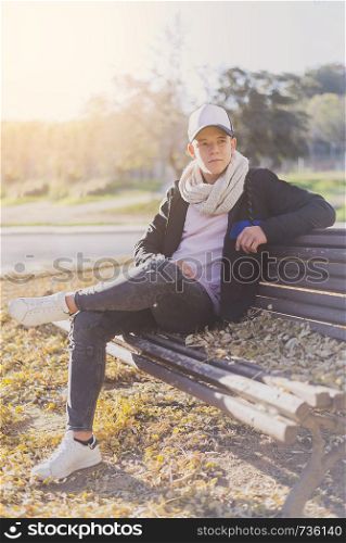 Stylish teenager sitting on a wooden bench on a city street casual wearing